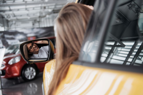 Молодая девушка смотрит в боковое зеркало автомобиля